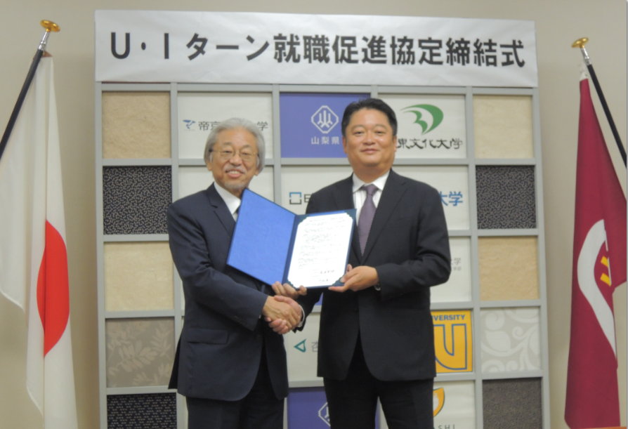 協定書を持ち握手する、長崎幸太郎・山梨県知事(右)と門脇廣文・大東文化大学学長(左)