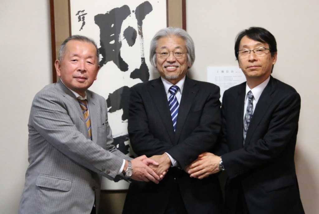 今後のさらなる連携を見据えて、ネクスコ東日本リテイルの金子社長（左側）とネクスコ東日本ロジテムの佐野社長（右側）の二人の社長が門脇学長としっかりと握手を交わす